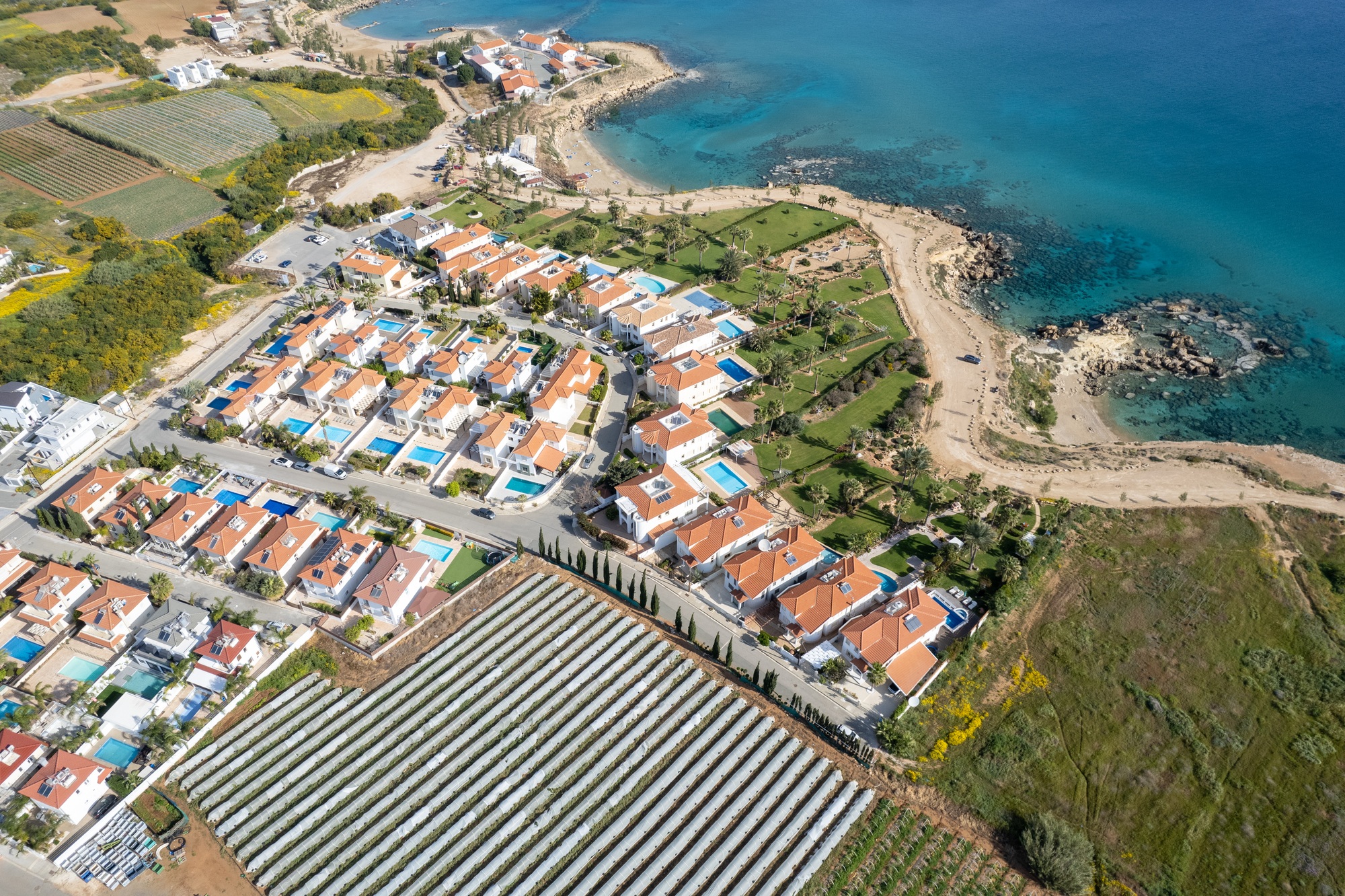 Drone aerial of holiday village with luxury houses at an idyllic rocky coast. Summer vacations at